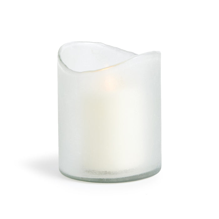 A clear glass hurricane with a melted edge and a candle inside, emitting a soft light.