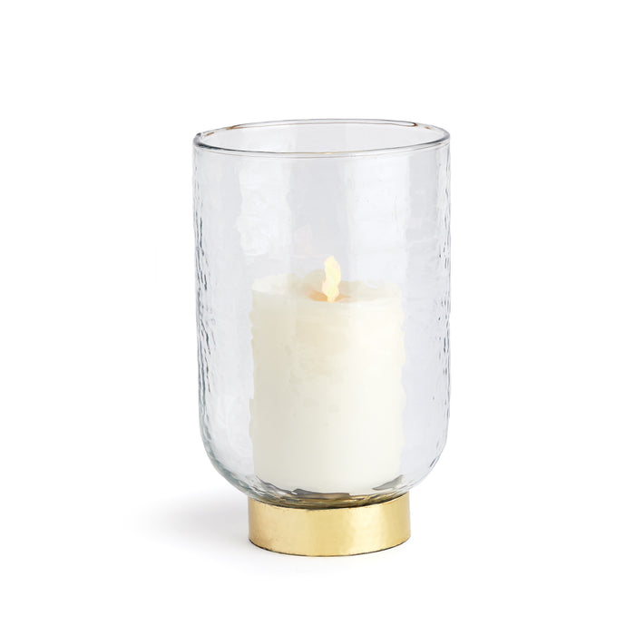 A clear glass hurricane candle holder with a gold hammered rim base, containing a lit candle.