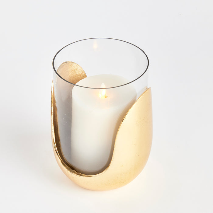 Gold-toned crescent candle holder with a white pillar candle inside a clear glass cylinder.