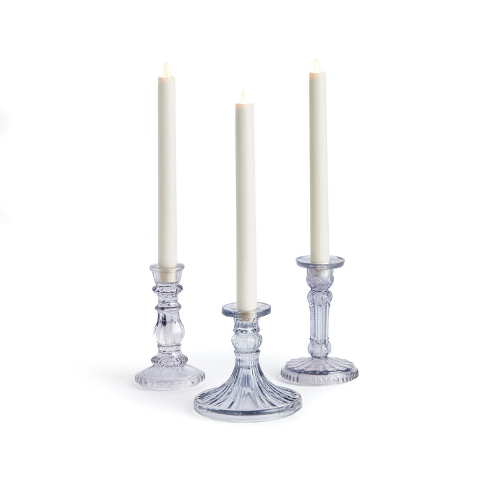 A set of three clear glass taper candle holders, each with a lit candle inside, set against a white background.