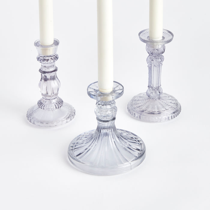 Set of three small clear glass taper candle holders with ribbed stems and circular bases on white background