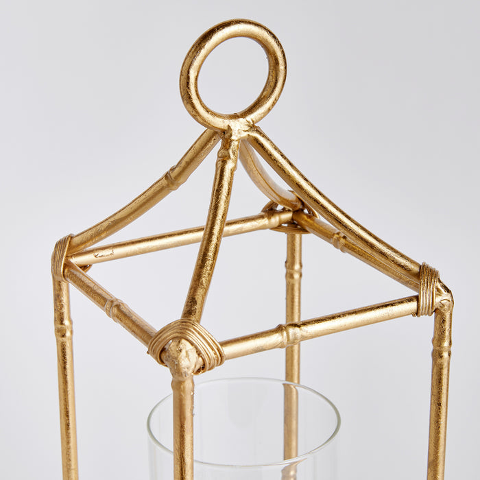 Gold metal geometric lantern with ring top, glass candle holder, and wrapped joints on a light gray background.