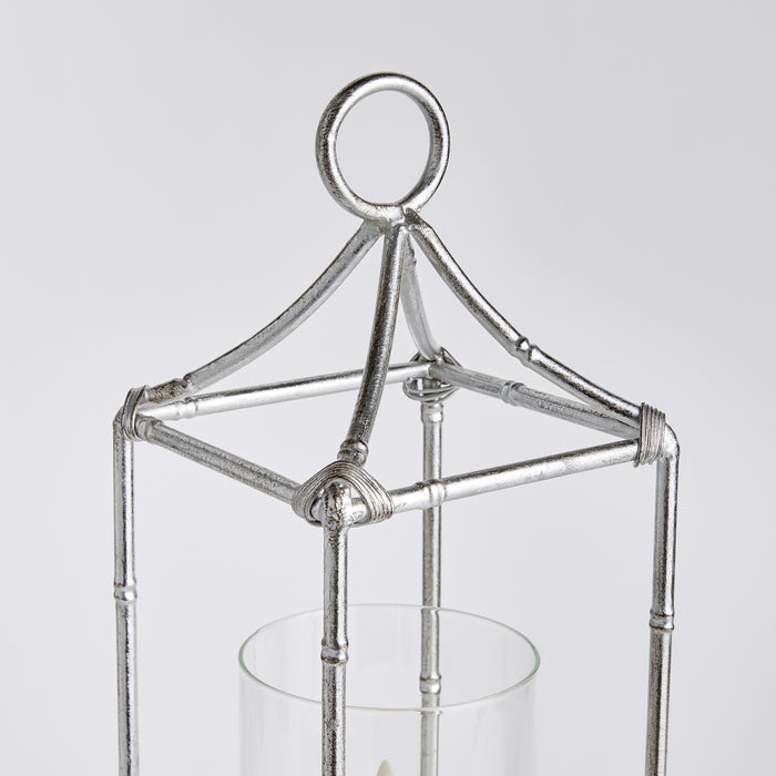 Silver metal lantern frame with glass hurricane holder, ring top, and triangular framework on a light background.