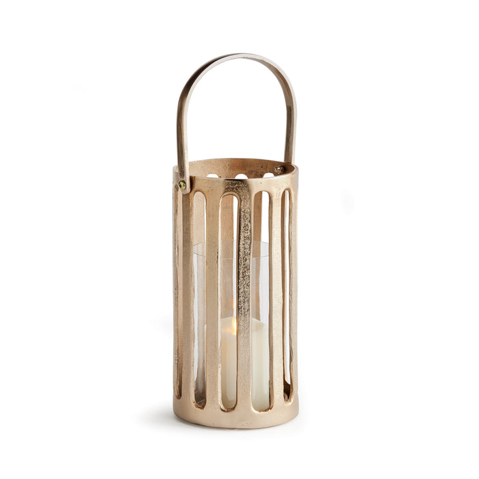 A champagne gold finish cast aluminum hurricane with a clear glass insert and a candle lit inside, set against a white background.