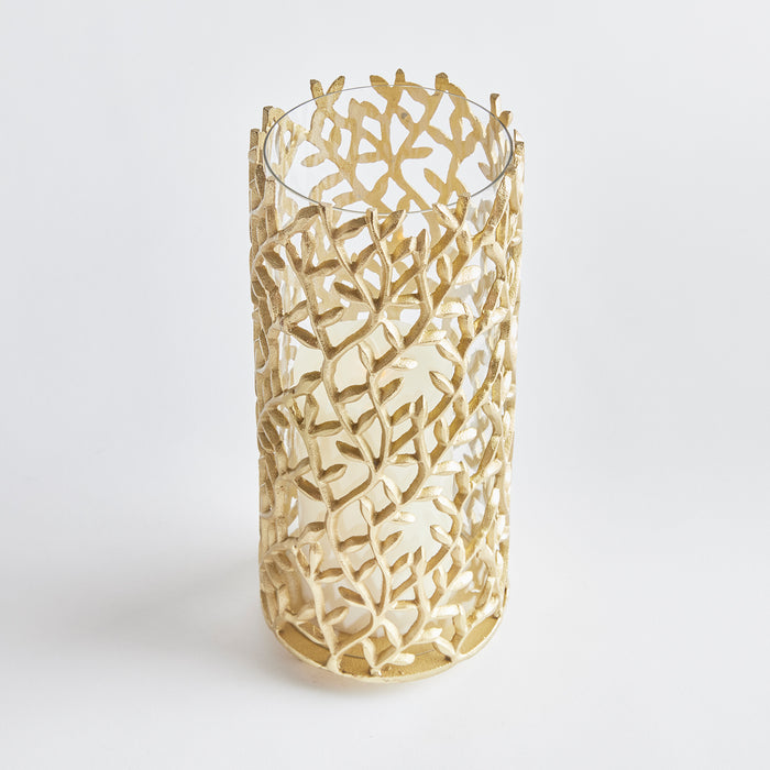 Gold leaf-like lattice hurricane candle holder with intricate cutout branches surrounding a white candle, cylindrical with