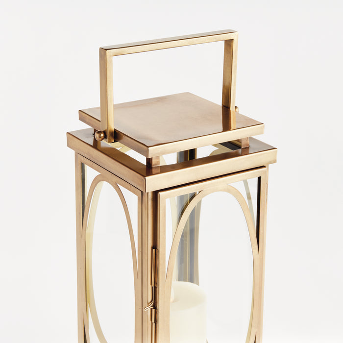Gold-toned metal lantern with glass panels, arched-frame doors, and a square handle on top, candle inside.