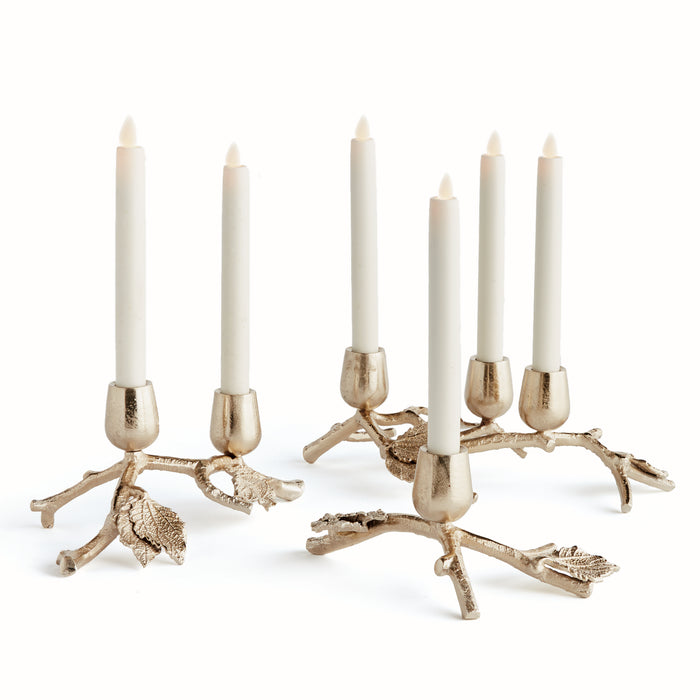 A set of three gold-colored aluminum candle holders with a nature-inspired branch and leaf design, holding three lit candles each.