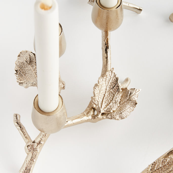 Set of three gold-toned taper candle holders with leaf and branch motifs on a white background.