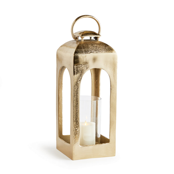 Gold-tone lantern with open arched sides, glass hurricane containing a pillar candle, loop handle on top, standing on a