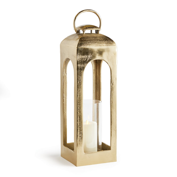 Gold lantern with a tall rectangular frame, glass sides, cylindrical candle inside, and a curved top handle on a white