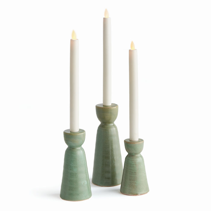 A set of three green stoneware candle holders with a tapered design, each holding a lit candle.