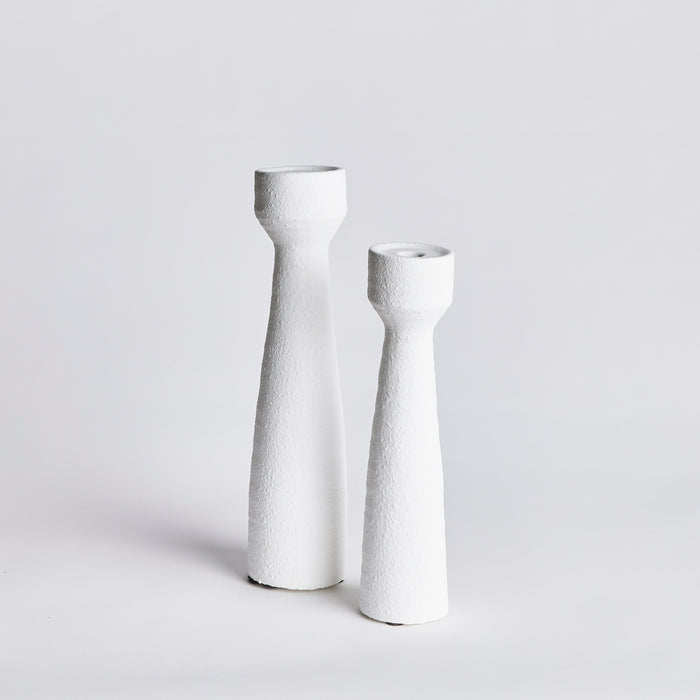 Set of two tall, white textured candlesticks with narrow, tapered bodies and round bases on a light gray background.