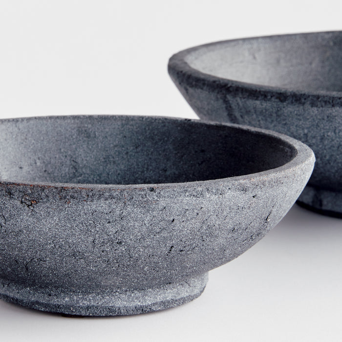 Set of two textured dark gray bowls with rough stone-like finish on light background