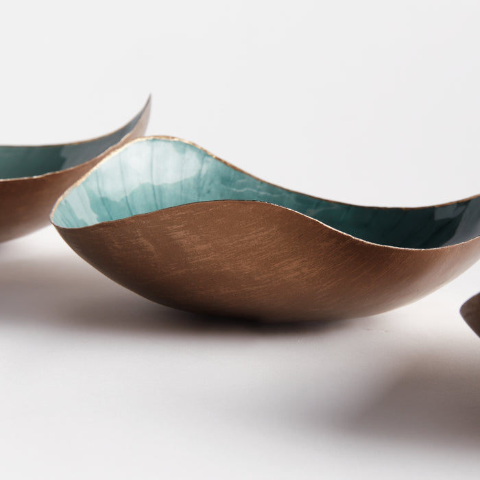 Set of three wavy bowls with copper exterior and teal interior, shallow leaf-like shapes on white background.