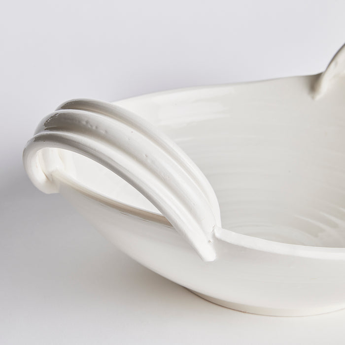 White ceramic decorative low bowl with curved double handles, glossy glaze, shallow dish, light gray background.