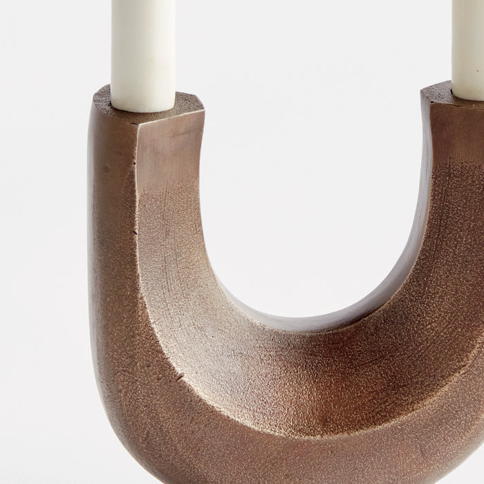 Brown U-shaped candelabra with two ivory candles, textured ceramic finish, neutral backdrop.