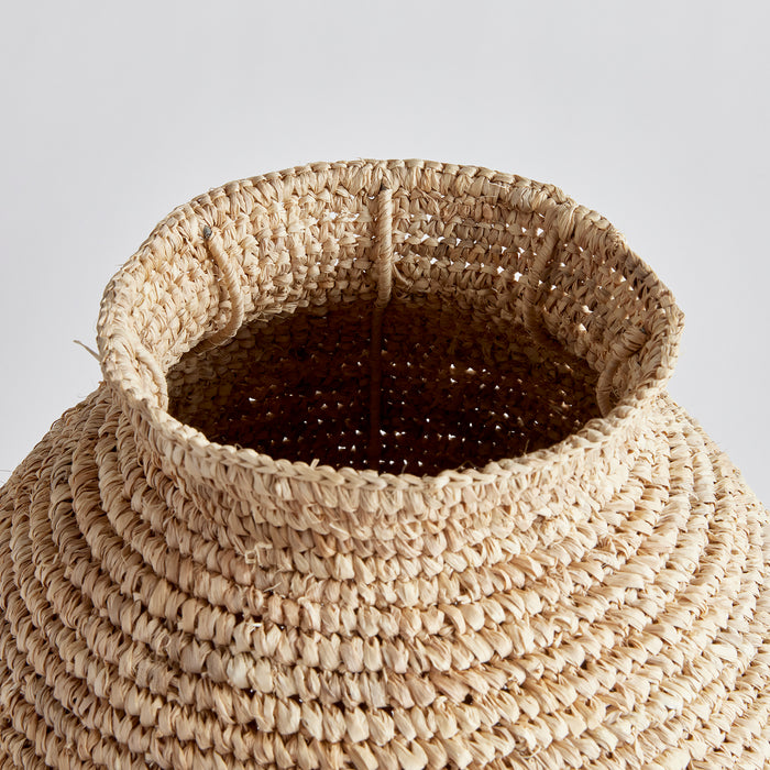 Small woven vase with natural straw fibers, round brim, and open top against a light gray background.