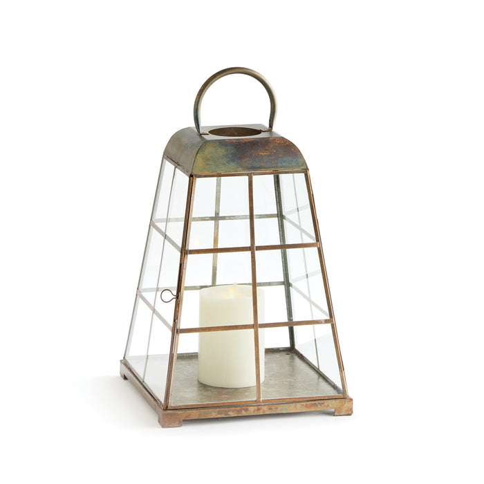 A small lantern with a modern tapered silhouette, featuring upright handles and a warm antique brass finish, designed for indoor use.