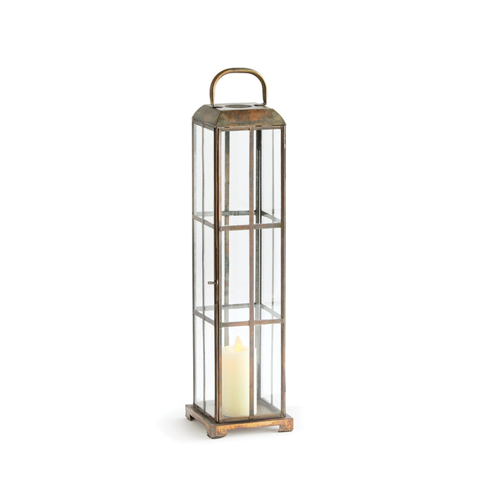 A tall, slender brass lantern with a geometric pattern of brass panes and a candle inside, designed for indoor use.