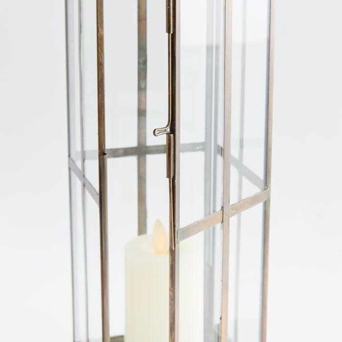 Rusty metal frame lantern with glass panels, small hook latch, candle inside, neutral background.