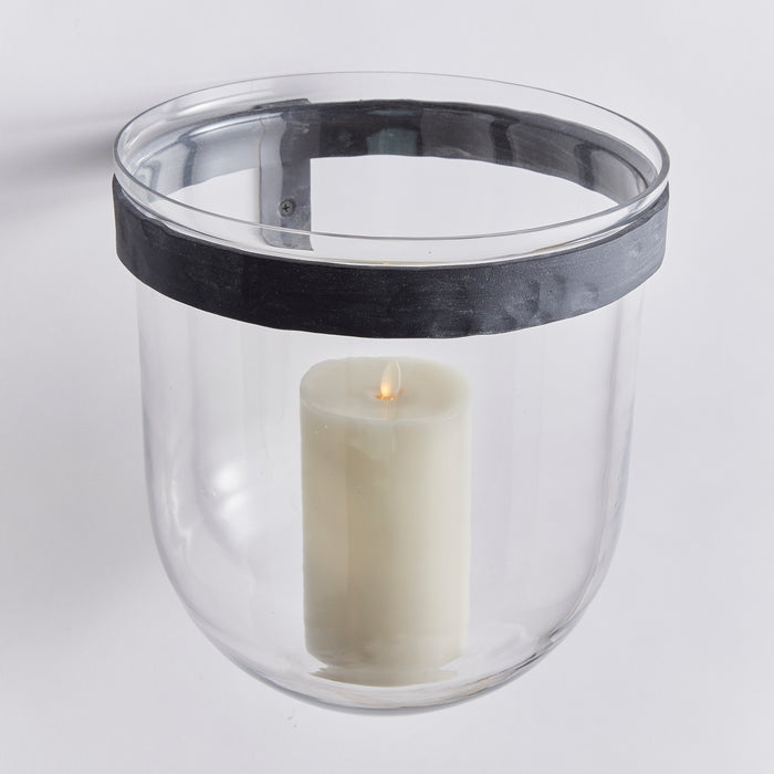 Clear glass wall-mounted vessel with a wide black metal band around the rim and a white pillar candle inside.