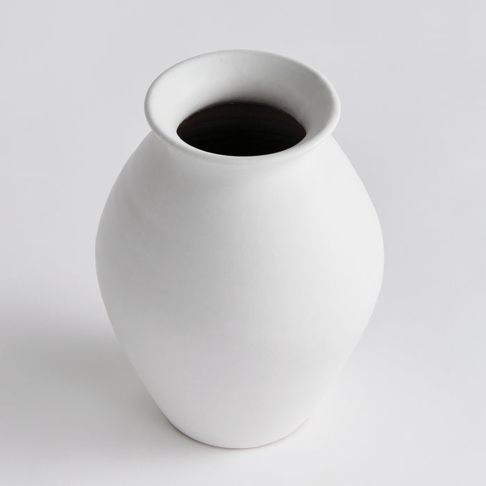 Small white ceramic vase with a rounded body and wide, flared neck, set on a light gray background.