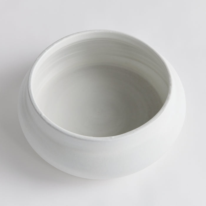 White ceramic decorative bowl with a smooth matte finish, round shape, wide rim, empty interior on light gray background.