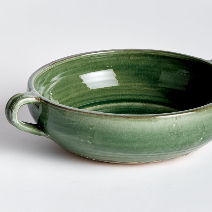 Green glazed ceramic decorative bowl with a small handle, shallow oval shape, crackled glaze, sits on light background.