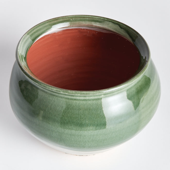 Round ceramic drum vase in green glaze with a red-brown interior, glossy crackled glaze, white base, on light background.