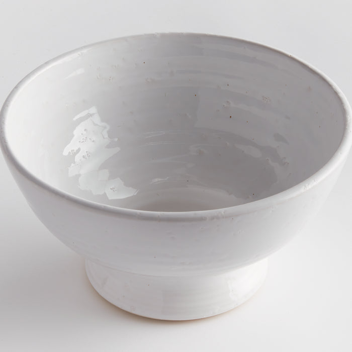 White ceramic decorative bowl with a wide rim and pedestal base, glossy glaze, empty inside, neutral background.