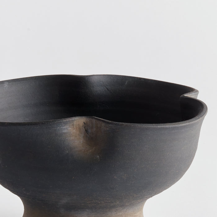 Large black ceramic decorative bowl with matte finish and organic wavy rim, set against light background.