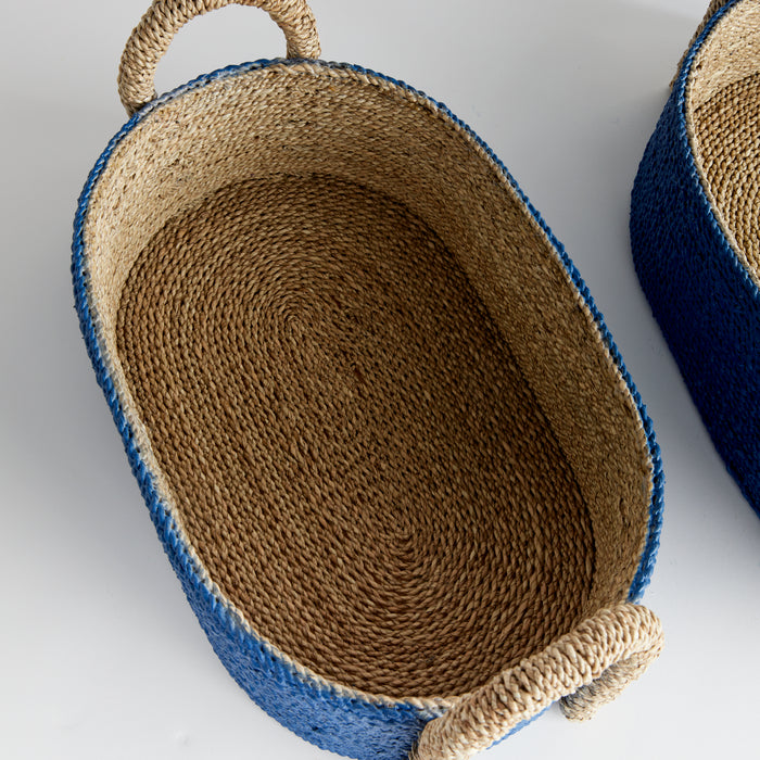 Two oval seagrass baskets with blue threaded rims and natural handles, interior natural straw color, set on white background