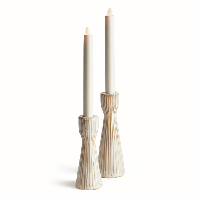 A pair of beige stoneware candle holders with a textured design, each holding a lit candle, set against a white background.