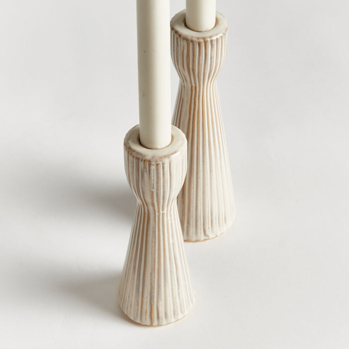 Set of two cream-toned taper candle holders with vertical ribbed texture on ceramic bases, empty candles, light gray