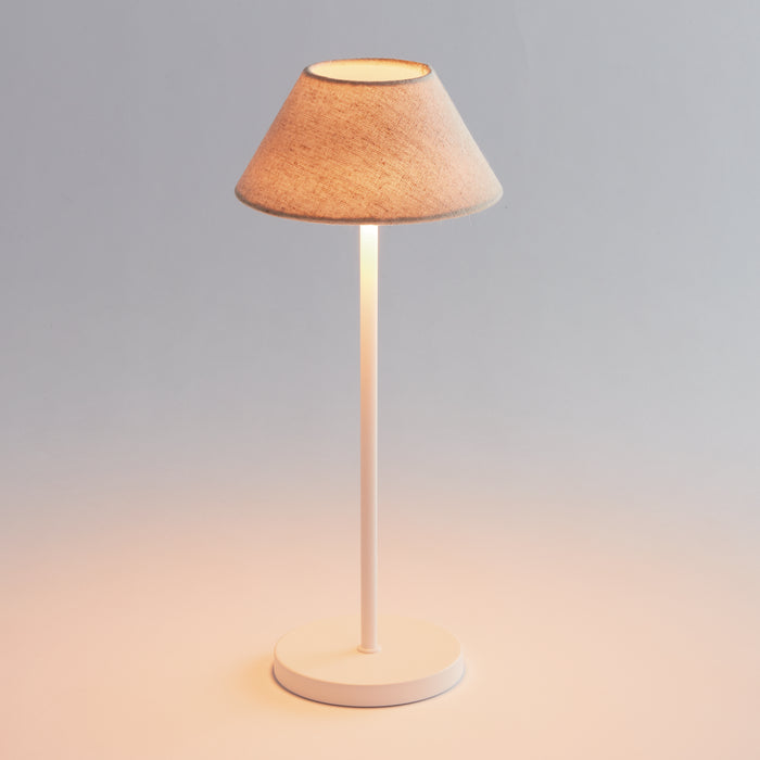 White cordless LED lamp with beige fabric lampshade on slim vertical stem and round base, illuminated against soft gray