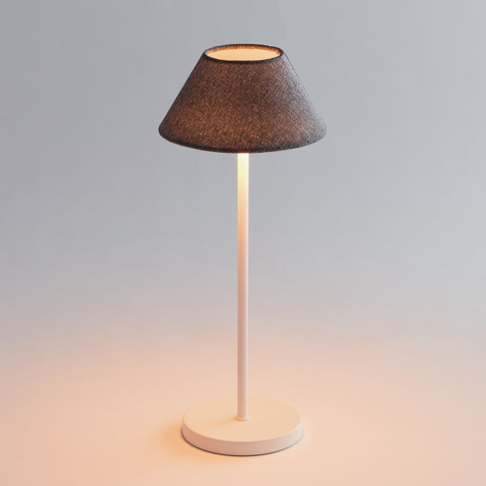 Cordless led lamp with white metal base and stem, dark fabric lampshade, warm light glow, simple background