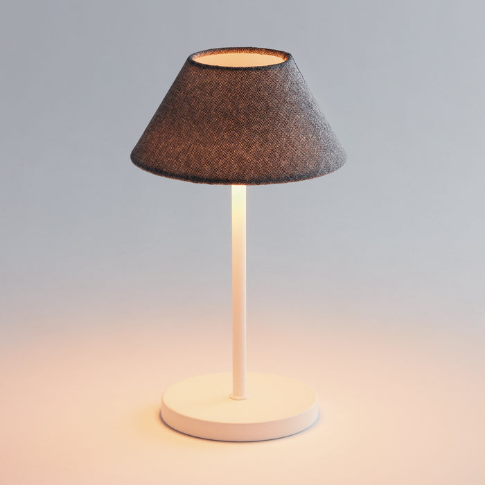 Cordless lamp with dark gray fabric cone shade, white cylindrical stem, round white base, warm light glow on surface