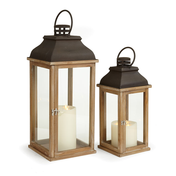 A set of two lanterns, one with a black rusted metal top and the other with a brown wooden top. Both have clear glass windows and are designed for holding candles.