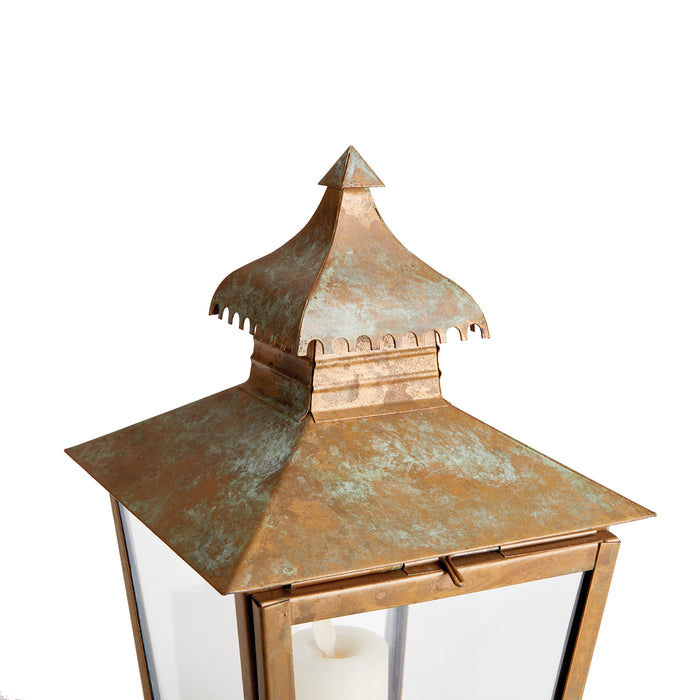 Copper-toned metal lantern with a patina finish, square glass panels, and a decorative tiered roof against a white
