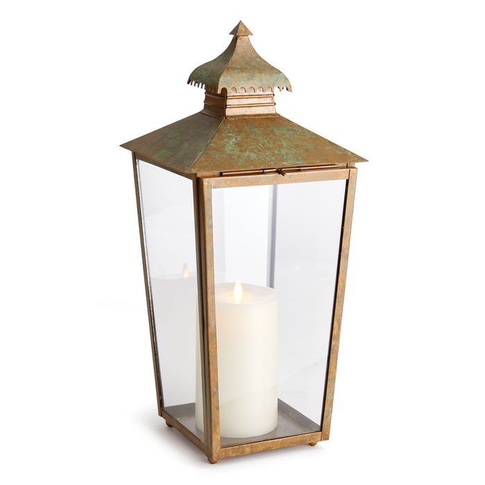 A bronze-colored lantern with a curved top and notched edges, featuring a glass enclosure and a candle inside.