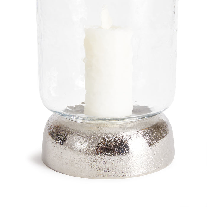 Clear glass hurricane with a white pillar candle, set on a textured metallic silver base.