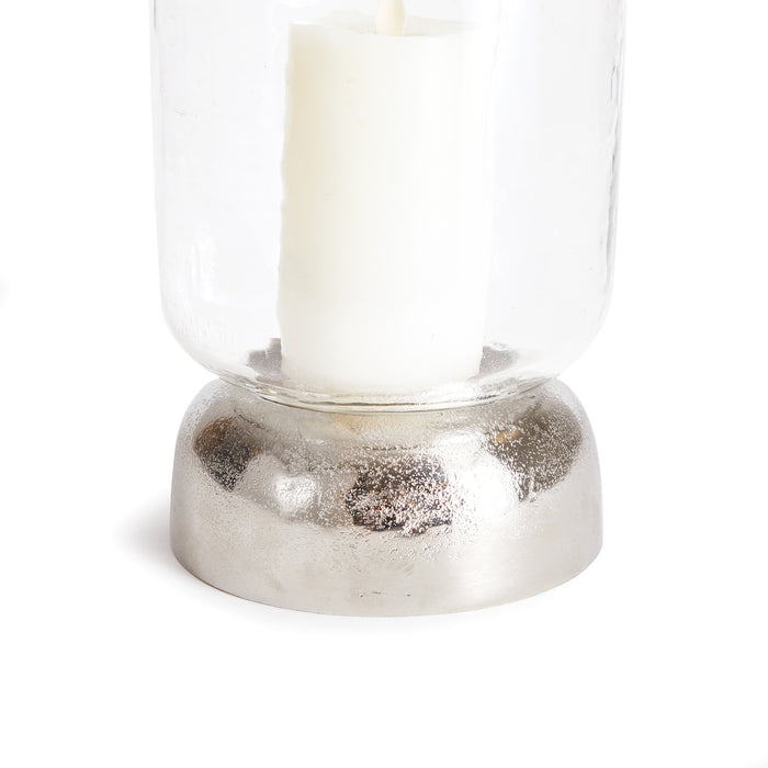 Hurricane candle holder with a clear glass body and a rounded metallic silver base, white pillar candle inside.