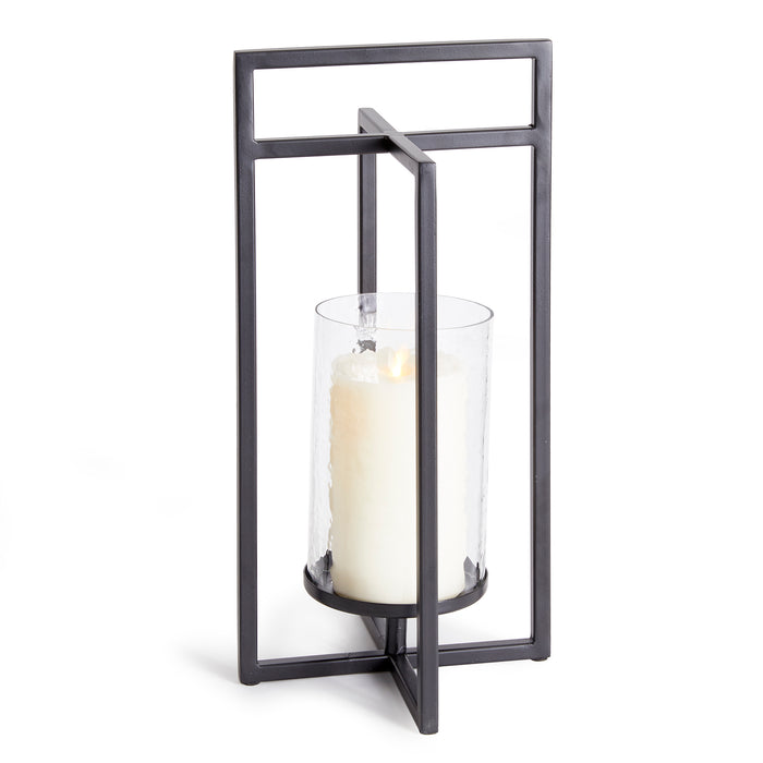 Industrial-style black metal lantern with a tall glass cylinder and white pillar candle inside, set against a white
