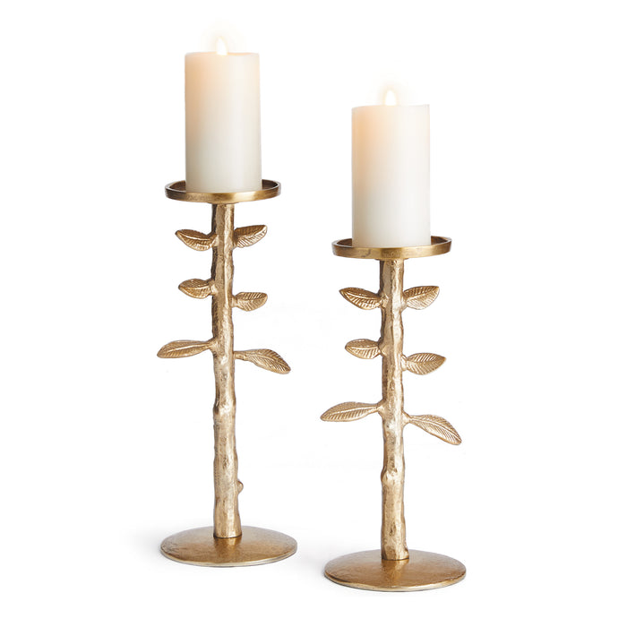 A set of two gold-colored candle stands with a branch-like design on each, holding cylindrical white candles.