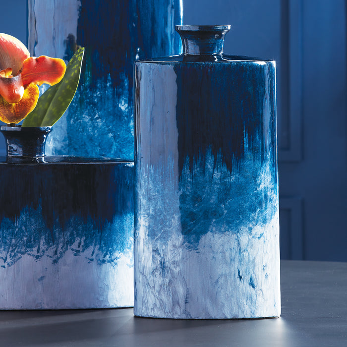 Small oval blue ceramic vase with glossy glaze, gradient dark to light blue, set on dark surface with background blues.