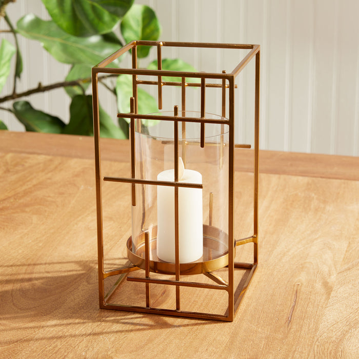 Copper metal geometric hurricane lantern with glass panels around a white pillar candle on a wooden table, warm indoor