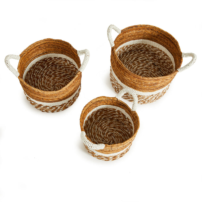 Set of three round woven baskets in natural brown and white with white rope handles, on white background.