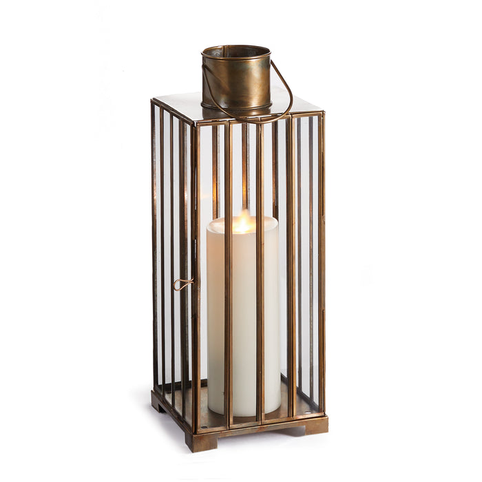 A small brass lantern with exaggerated brass panes designed to hold a candle. The lantern has a narrow shape and features a handle at the top for hanging.