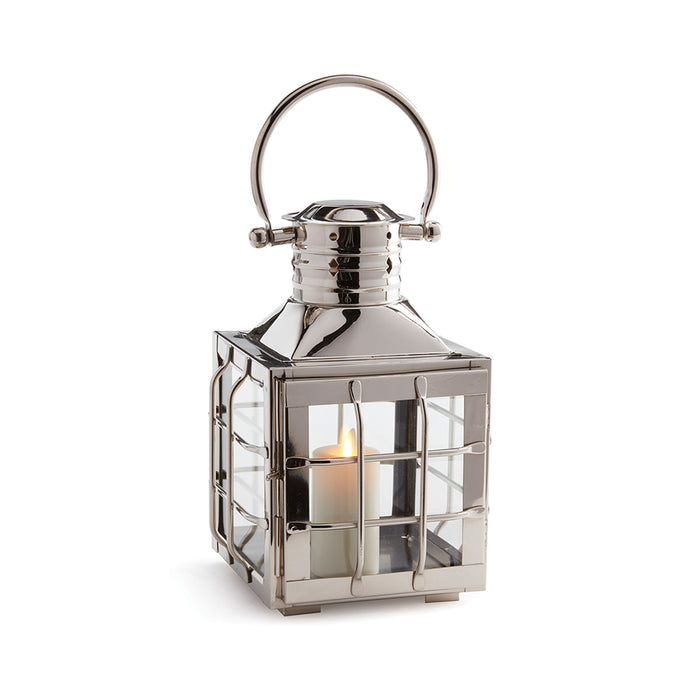 Shiny silver metal lantern with square frame, glass panels, protective grille, circular handle, lit candle inside, white