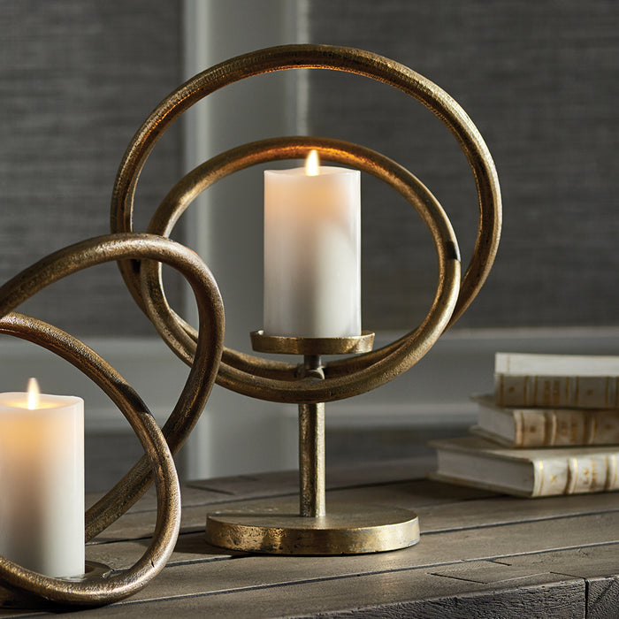 Design Shop Da Vinci Candleholder: antique brass circular loops with cylindrical white candle on a metal base, on wood